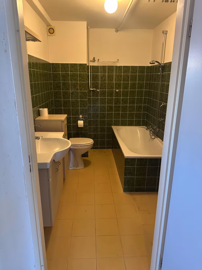 Verouderde badkamer met donkergroene tegels en een standaard ligbad in Alphen aan den Rijn.