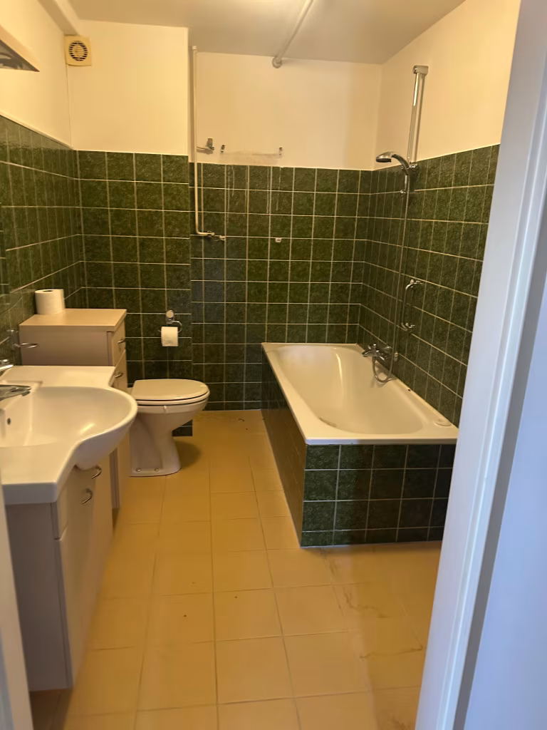 Verouderde badkamer met donkergroene tegels en een standaard ligbad in Alphen aan den Rijn.