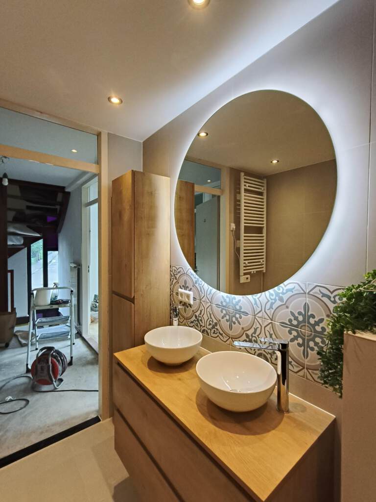 Moderne badkamer na renovatie – houten meubel, terrazzo wand en warme verlichting.
