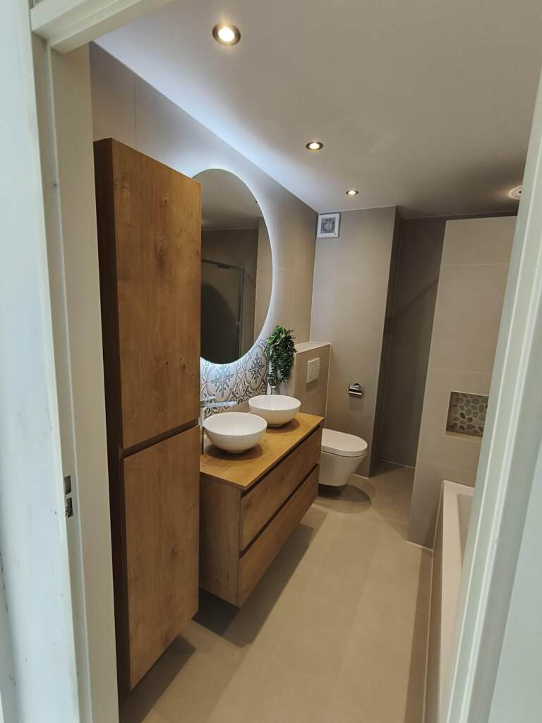 Moderne badkamer na renovatie – houten meubel, terrazzo wand en warme verlichting.