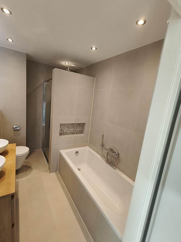 Moderne badkamer na renovatie – houten meubel, terrazzo wand en warme verlichting.