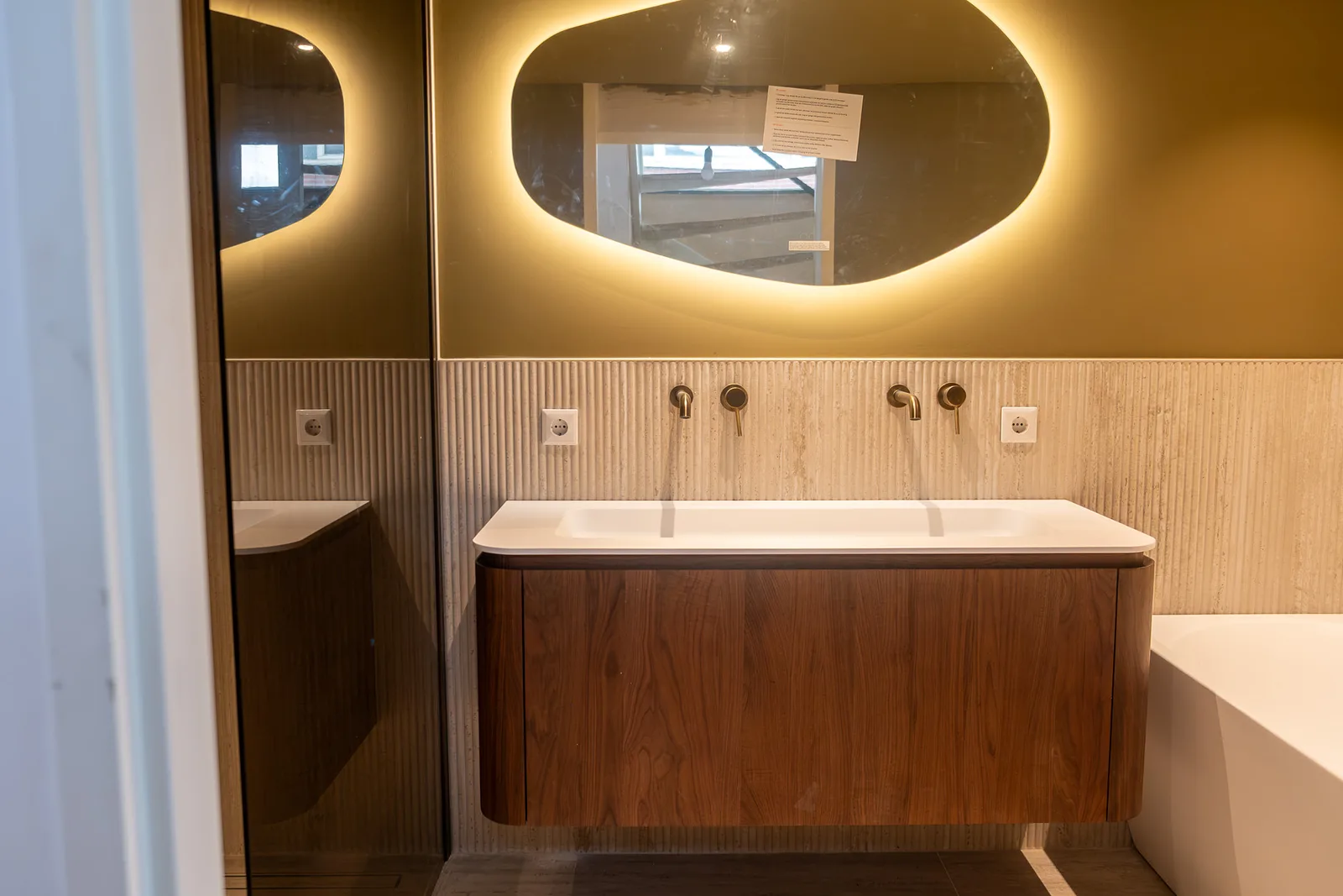 Badkamerrenovatie in Alphen aan den Rijn met dubbele wastafel, notenhouten badmeubel, travertijn ribbeltegels en messing kranen