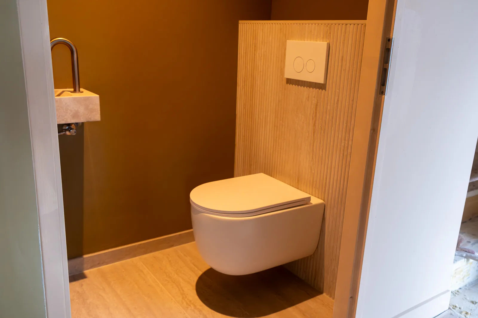 Modern hangtoilet met travertijn wandpaneel en fonteintje, toiletrenovatie door TNZ Aannemersbedrijf