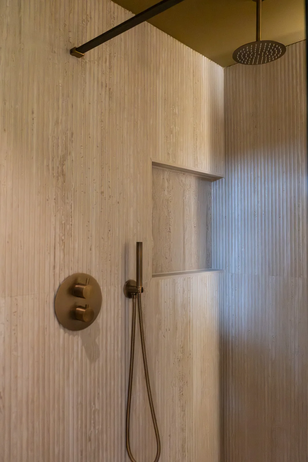 Regendouche met geborsteld messing thermostaatkraan en inbouwnis in travertijn wand